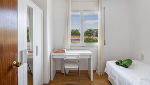 Une pièce avec un bureau, une chaise et un lit blancs, une fenêtre donnant sur un paysage agréable et une porte.