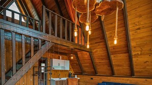 A spacious loft with a high ceiling, wooden beams, a staircase, a kitchen, a blue sofa, and a patterned rug. - Gezegen Bungalow (Sapanca)