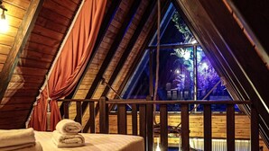 A cozy attic bedroom with a wooden ceiling, a bed with neatly folded towels, and a view of a lit outdoor area. - Gezegen Bungalow (Sapanca)