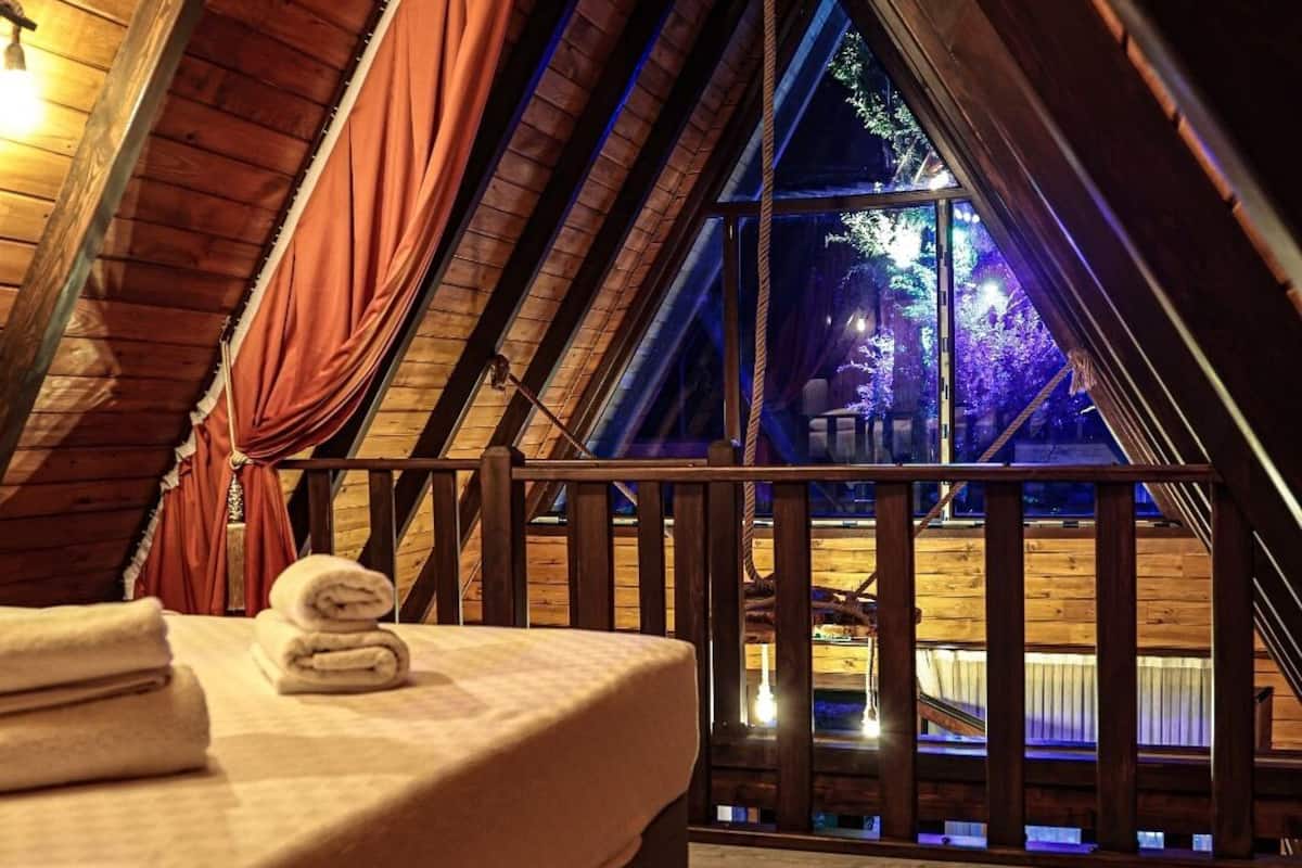 Een knus zolderkamer met houten plafond, een bed met netjes opgevouwen handdoeken, en uitzicht op een verlicht buitengebied.