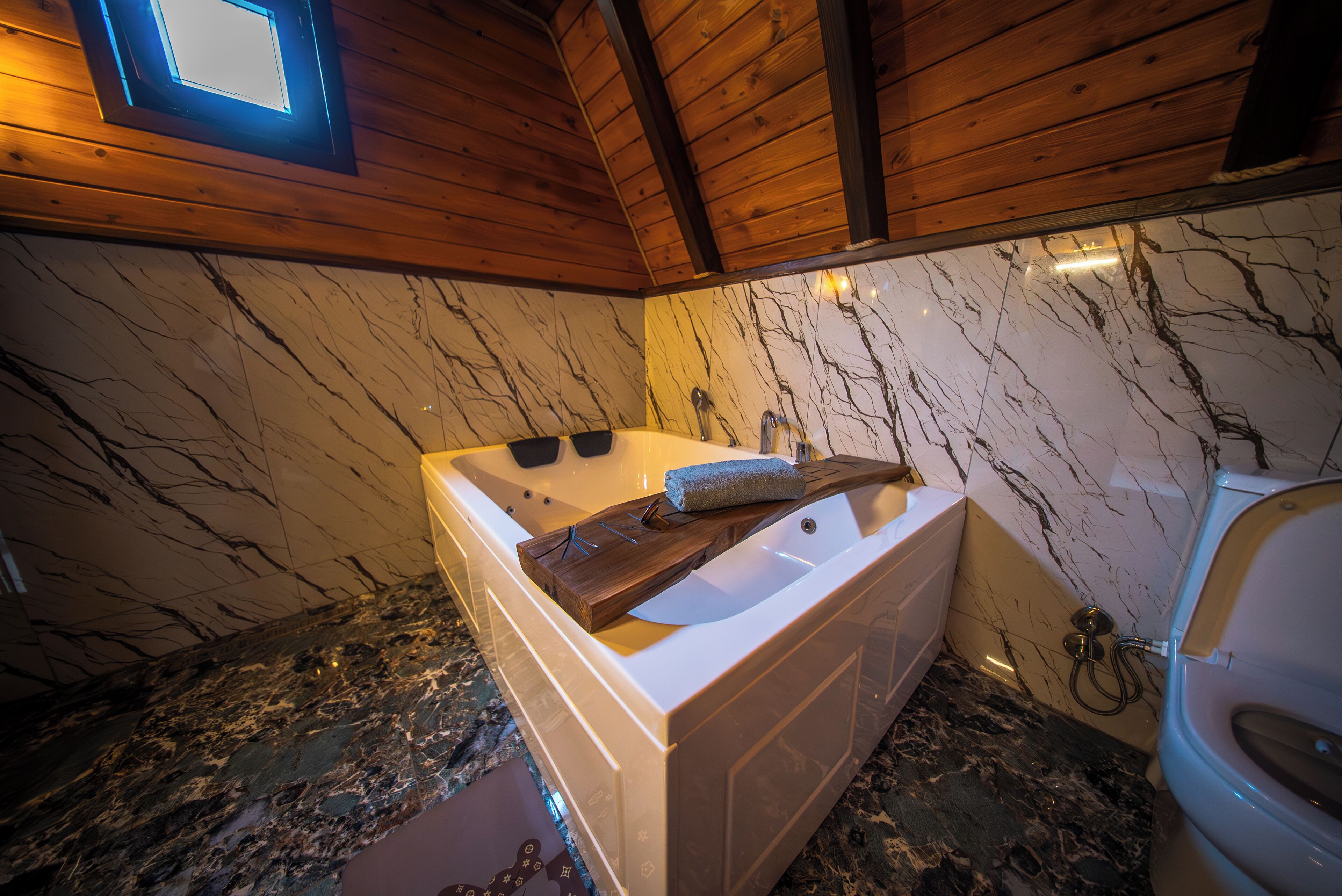 A bathroom with a marble wall, a wooden ceiling, a bathtub, and a toilet.