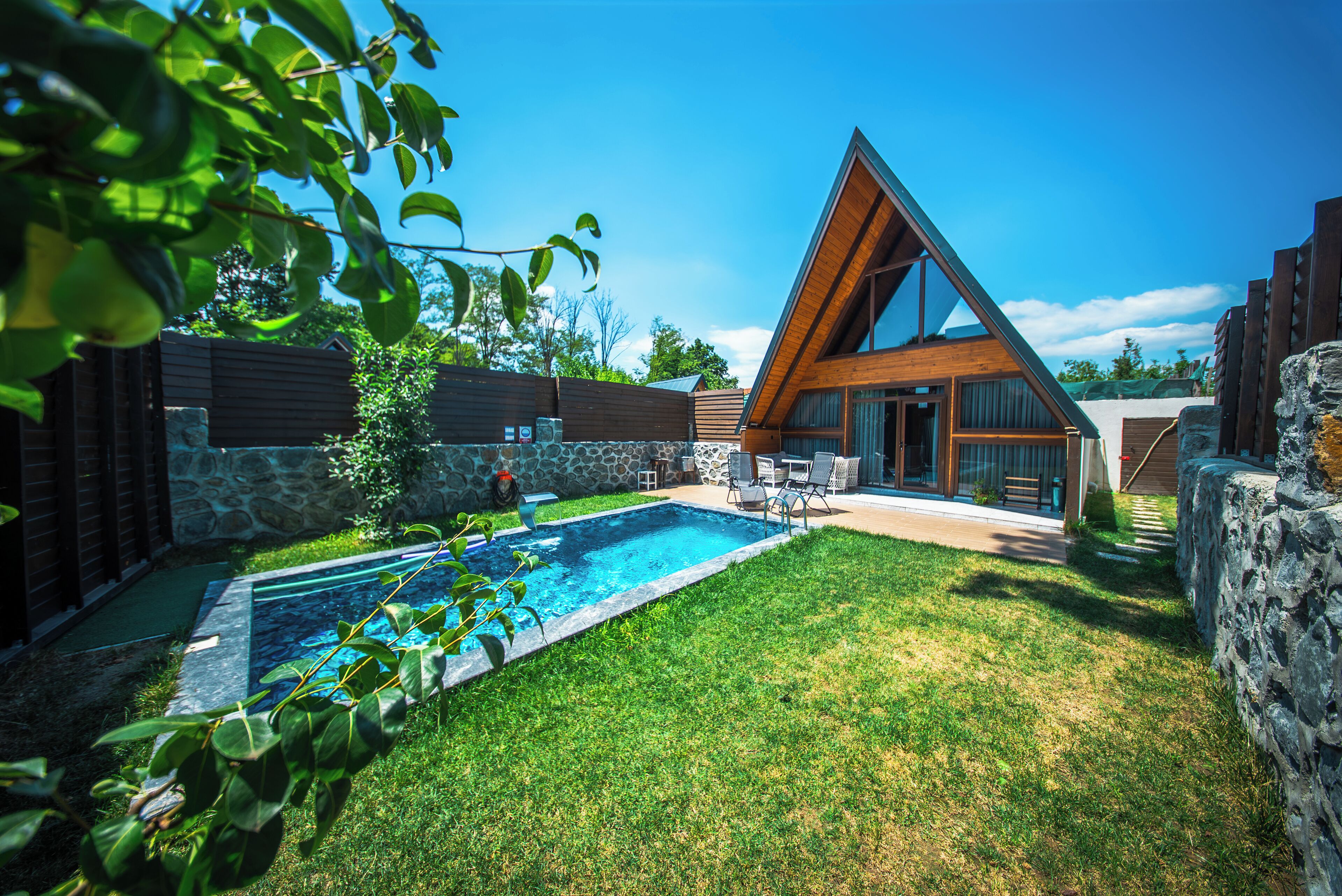 Una casa moderna amb piscina, parets de pedra i un jardí ben cuidat.