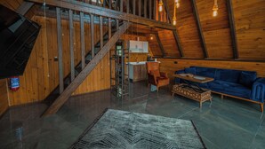 A spacious loft with a high ceiling, wooden beams, a staircase, a kitchen area, a blue sofa, and a patterned rug. - Gezegen Bungalow (Sapanca)