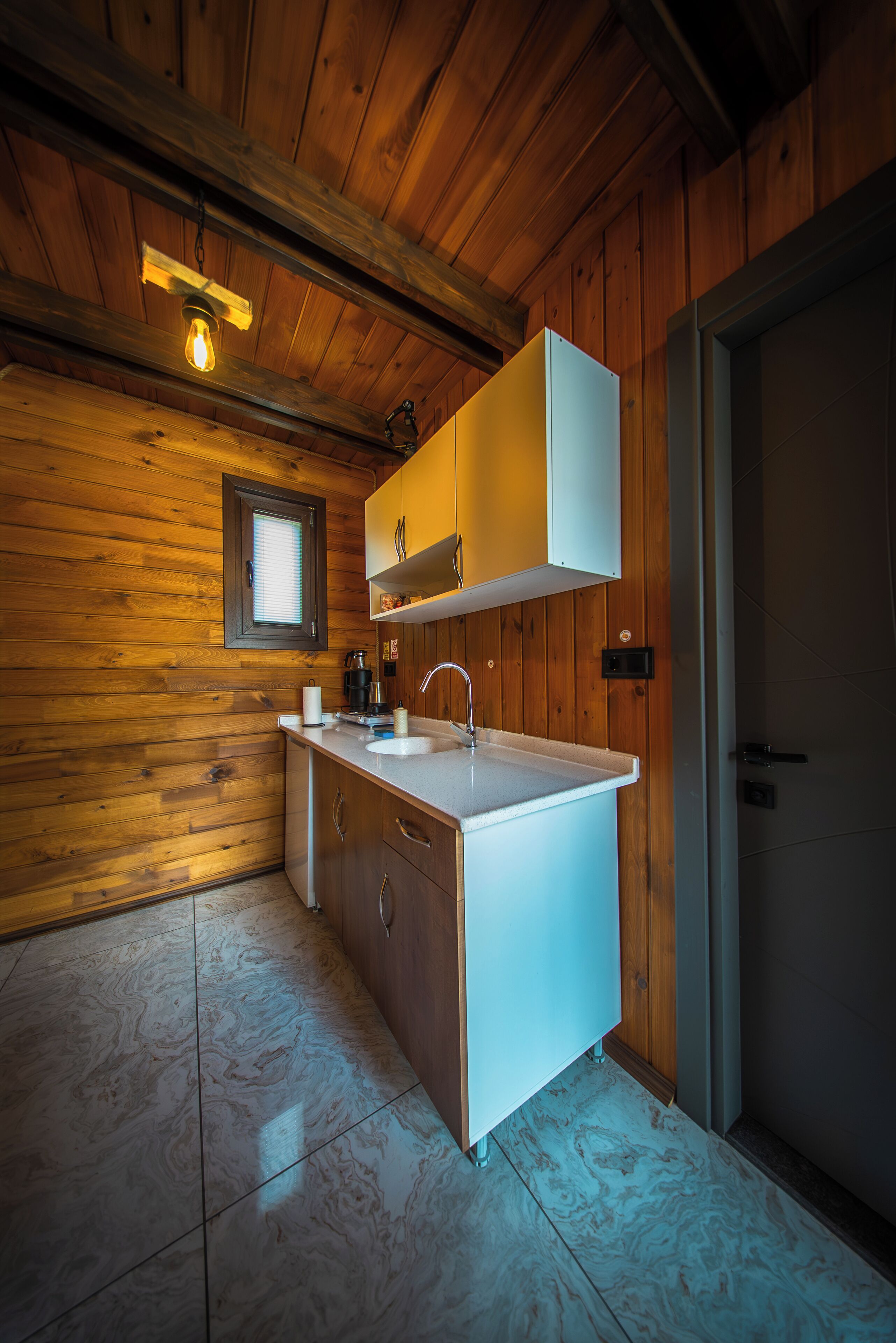 A wooden-paneled kitchen with a white countertop, a hanging light fixture, and a window above the sink.