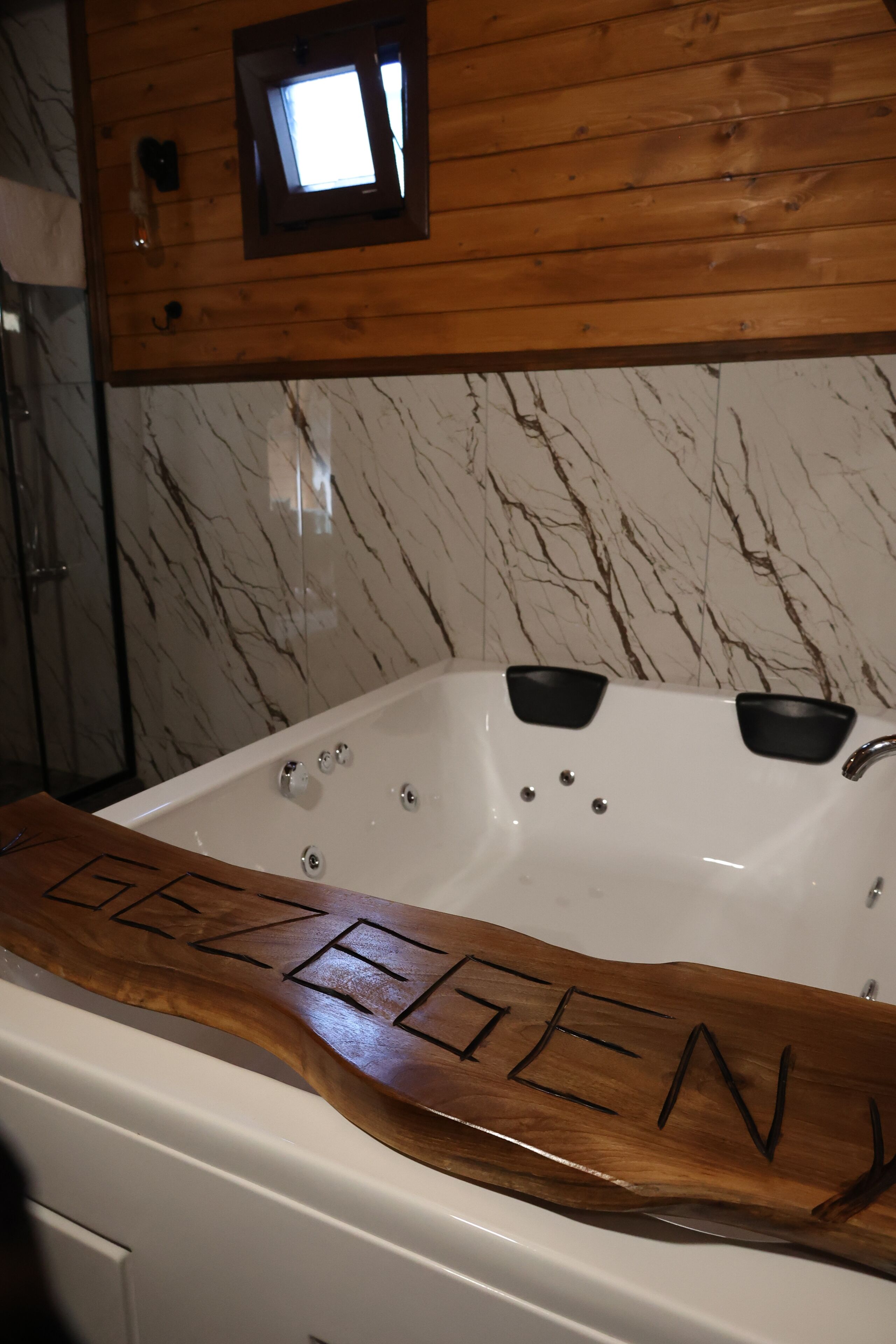 A bathroom with a marble wall, a wooden vanity, and a bathtub with the name 'DEZELEN' carved into the side.