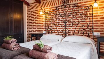 A room with a brick wall, a bed with white bedding, two rolled towels with greenery, and a decorative metal headboard.