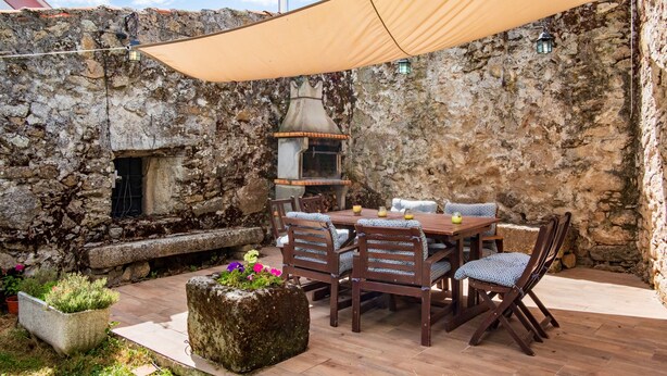 Un muro de piedra, asientos al aire libre, una mesa con sillas y una chimenea.
