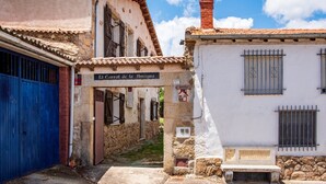 Una calle estrecha con edificios, una reja azul y un letrero que dice 'El Corral de la Antigua'.