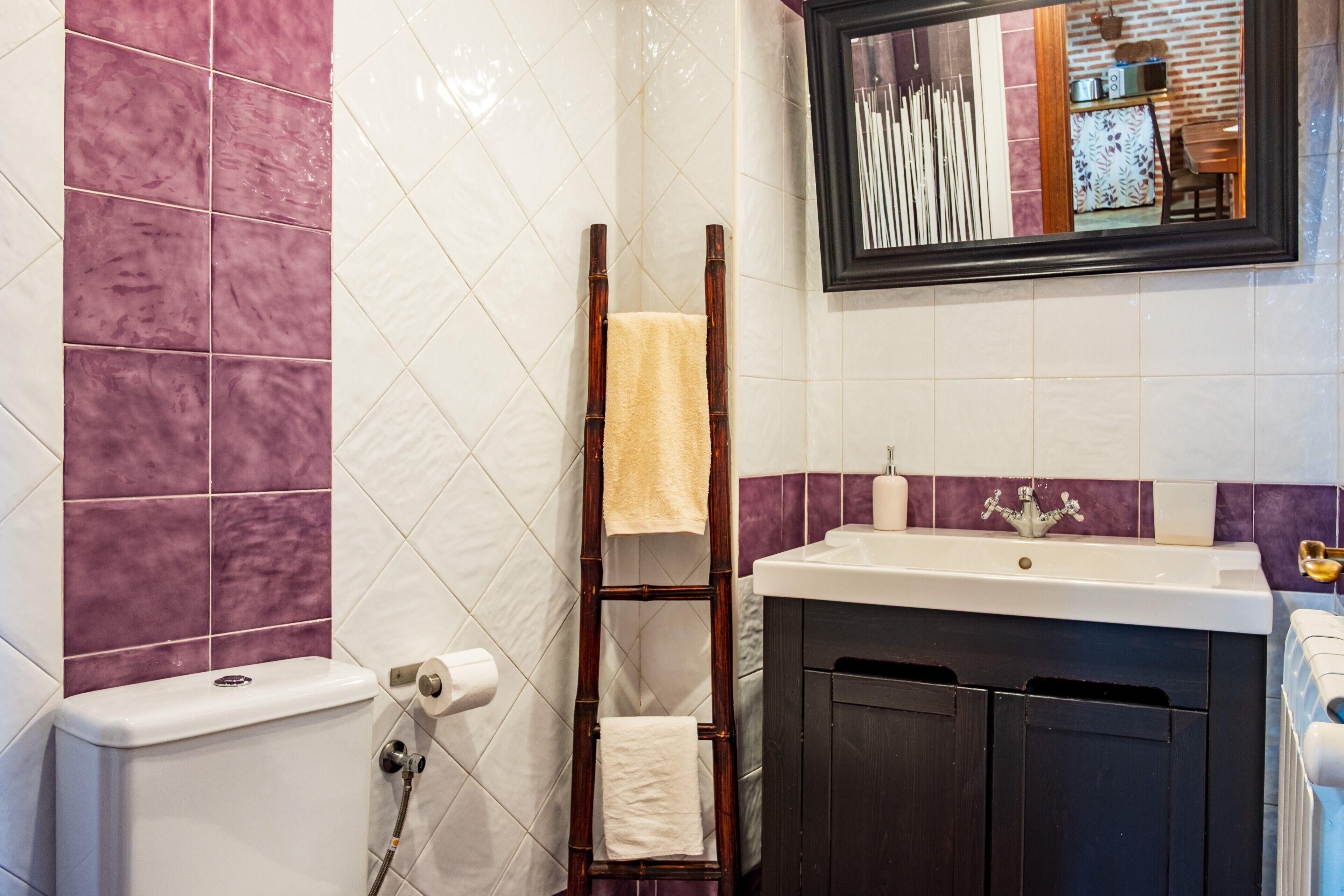 Un bagno con WC, lavabo e doccia. Una scala di legno con un asciugamano appoggiata al muro.