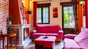 Una habitación acogedora con chimenea, un sofá rojo, una mesita y una ventana con cortinas.