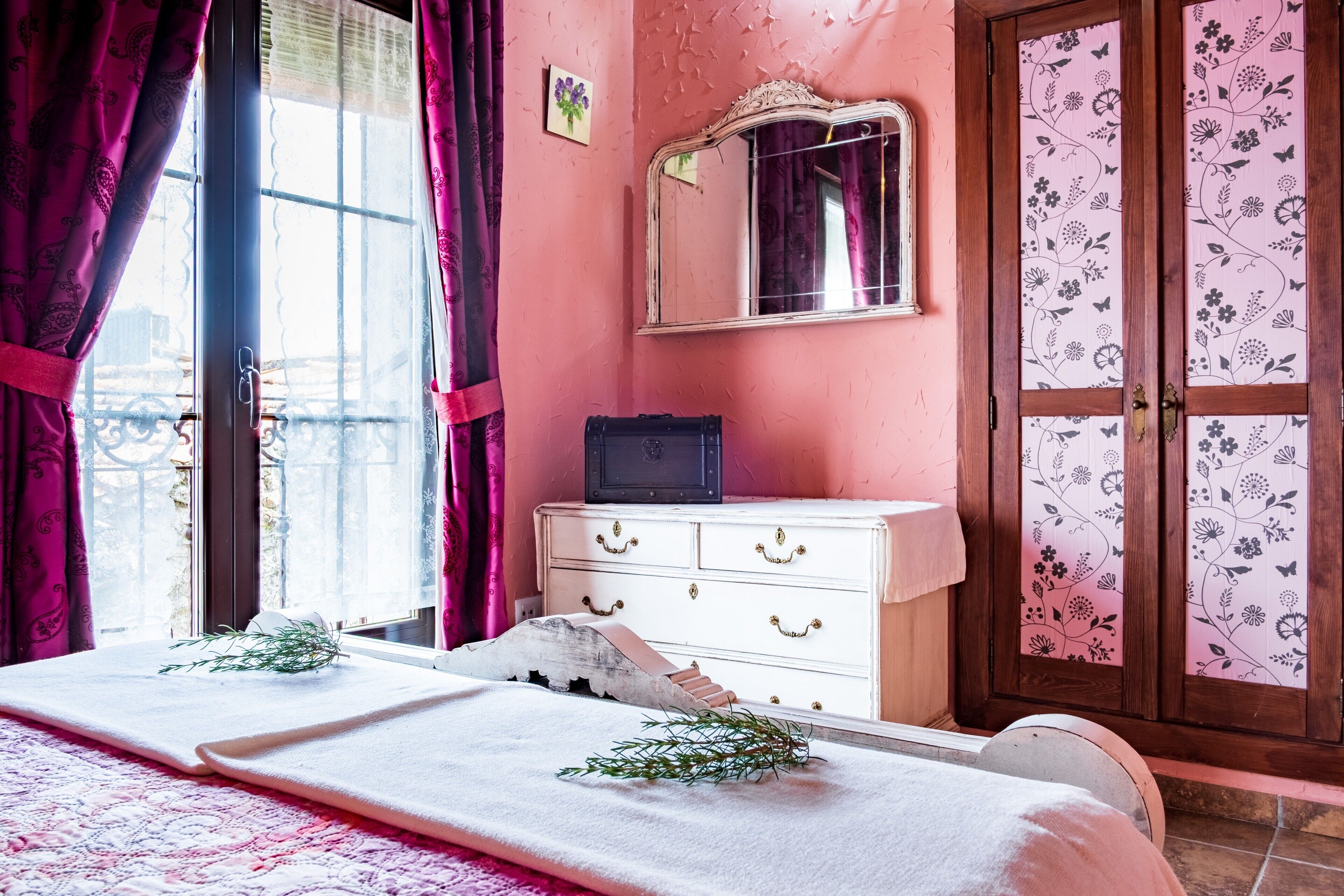 Una habitación con cama, cómoda, espejo y ventana con cortinas.