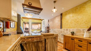 A kitchen with a brick wall, wooden cabinets, a tiled floor, and a hanging light fixture.