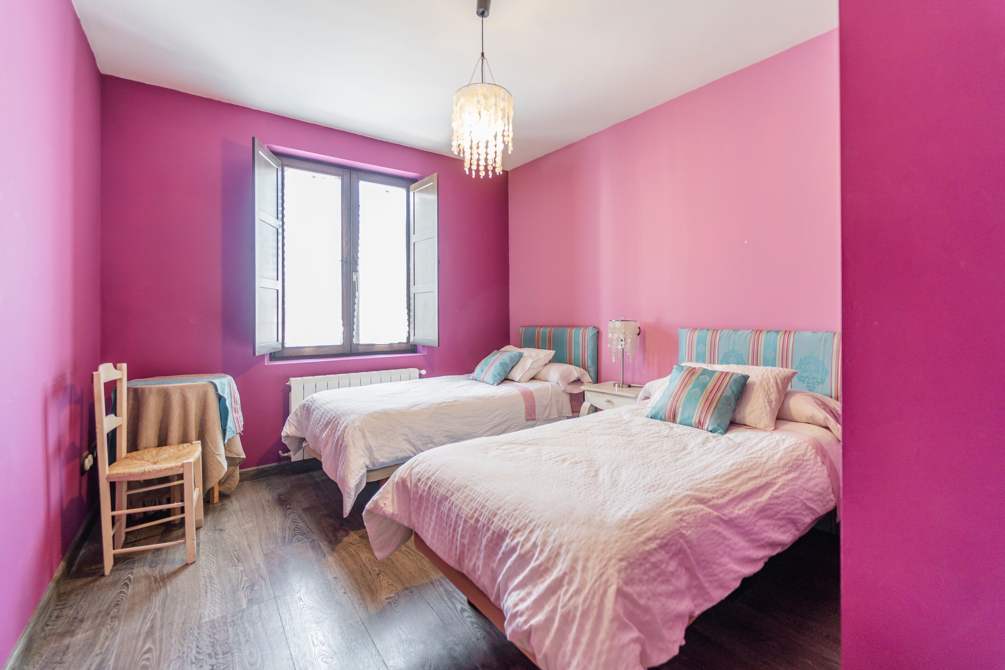 A room with two beds, a chair, a window, and a chandelier.