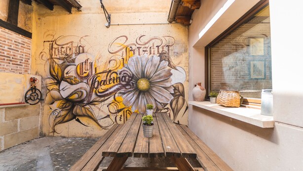 A wooden table with a potted plant in the center, set against a wall with graffiti art.