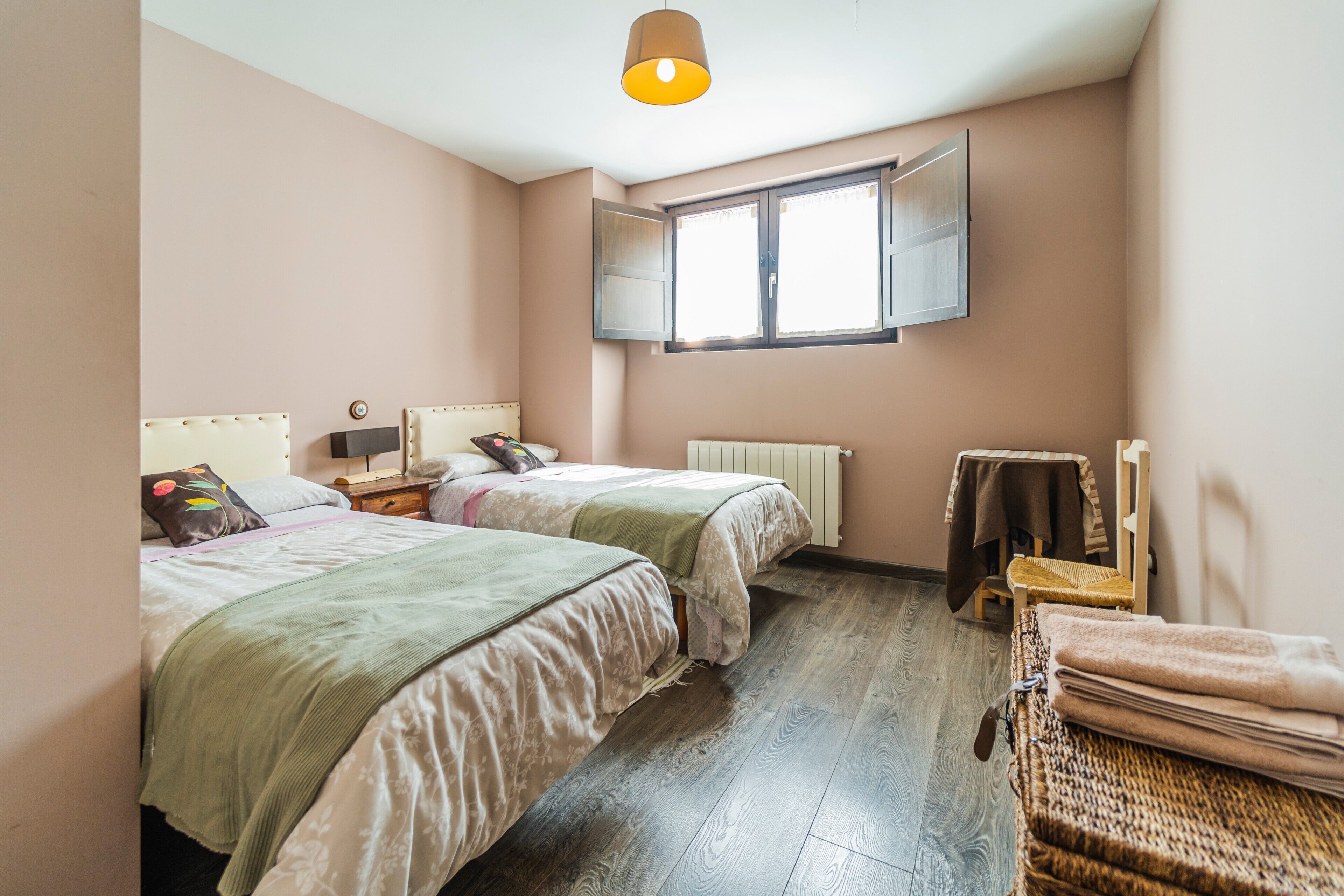 Une chambre avec deux lits, une fenêtre, un radiateur et un plancher en bois.