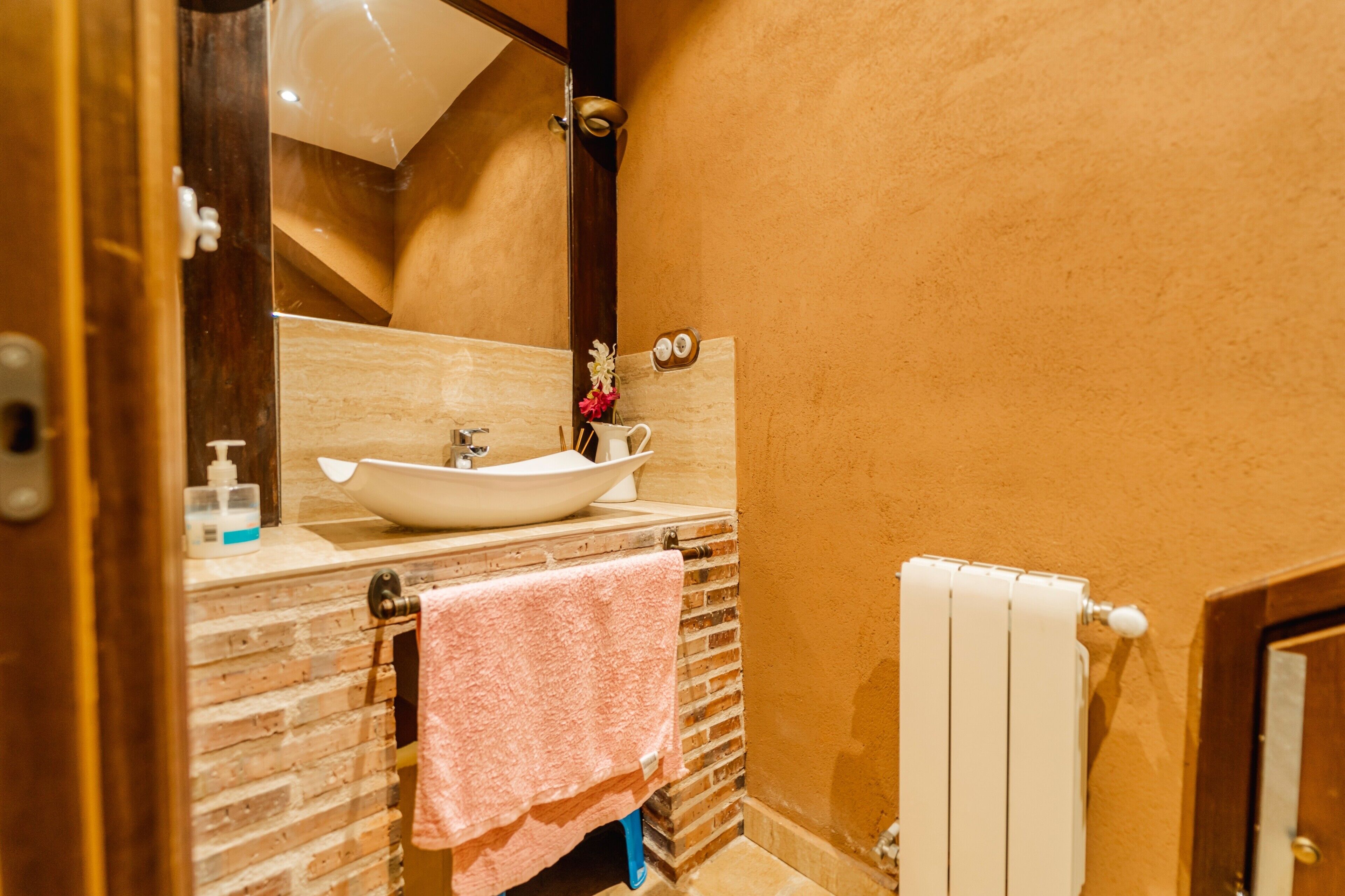 Un bagno con un lavabo a incasso bianco, uno specchio, un porta asciugamani e un termosifone.