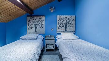 A bedroom with two beds, a nightstand, a wall-mounted lamp, and two tree-themed wall art pieces.