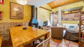 A dining area with a wooden table and chairs, a fireplace, a television, and a window with a view of the outside.