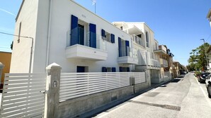 Un edificio bianco con persiane blu, un ingresso con cancello e un cielo sereno.