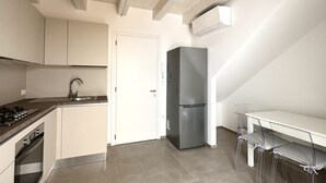 Una cucina moderna con frigorifero in acciaio inox, un piano di lavoro bianco e una zona pranzo con sedie trasparenti.