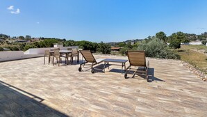 Une terrasse extérieure avec des fauteuils et une table, offrant une vue sur un paysage vallonné parsemé de maisons.