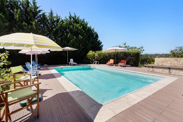 A swimming pool with lounge chairs and umbrellas, surrounded by a wooden deck and greenery.