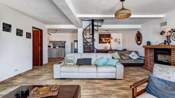 A spacious living room with a sofa, coffee table, and fireplace. A spiral staircase leads to an upper level.
