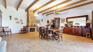 A spacious living area with a wooden dining table, chairs, a fireplace, and a kitchen area with cabinets and a large mirror.
