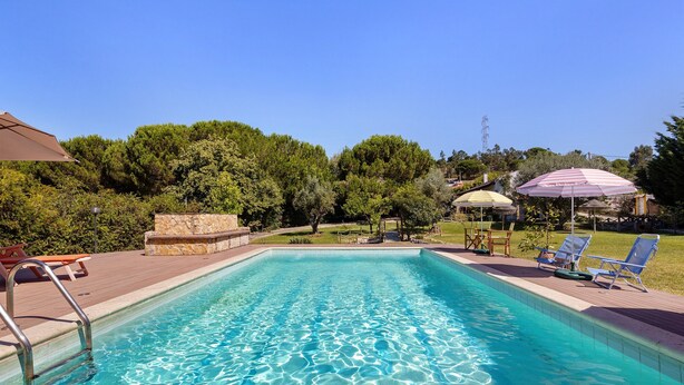 A rectangular swimming pool with clear blue water, surrounded by a stone deck, and shaded by umbrellas. - Apartment 'Casa Retiro' with Shared Pool, Wi-Fi and Air Conditioning (Azambuja)