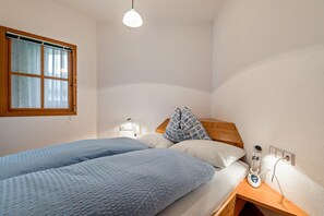 Un dormitorio con dos camas, una mesita de noche, una lámpara, una ventana y un enchufe.