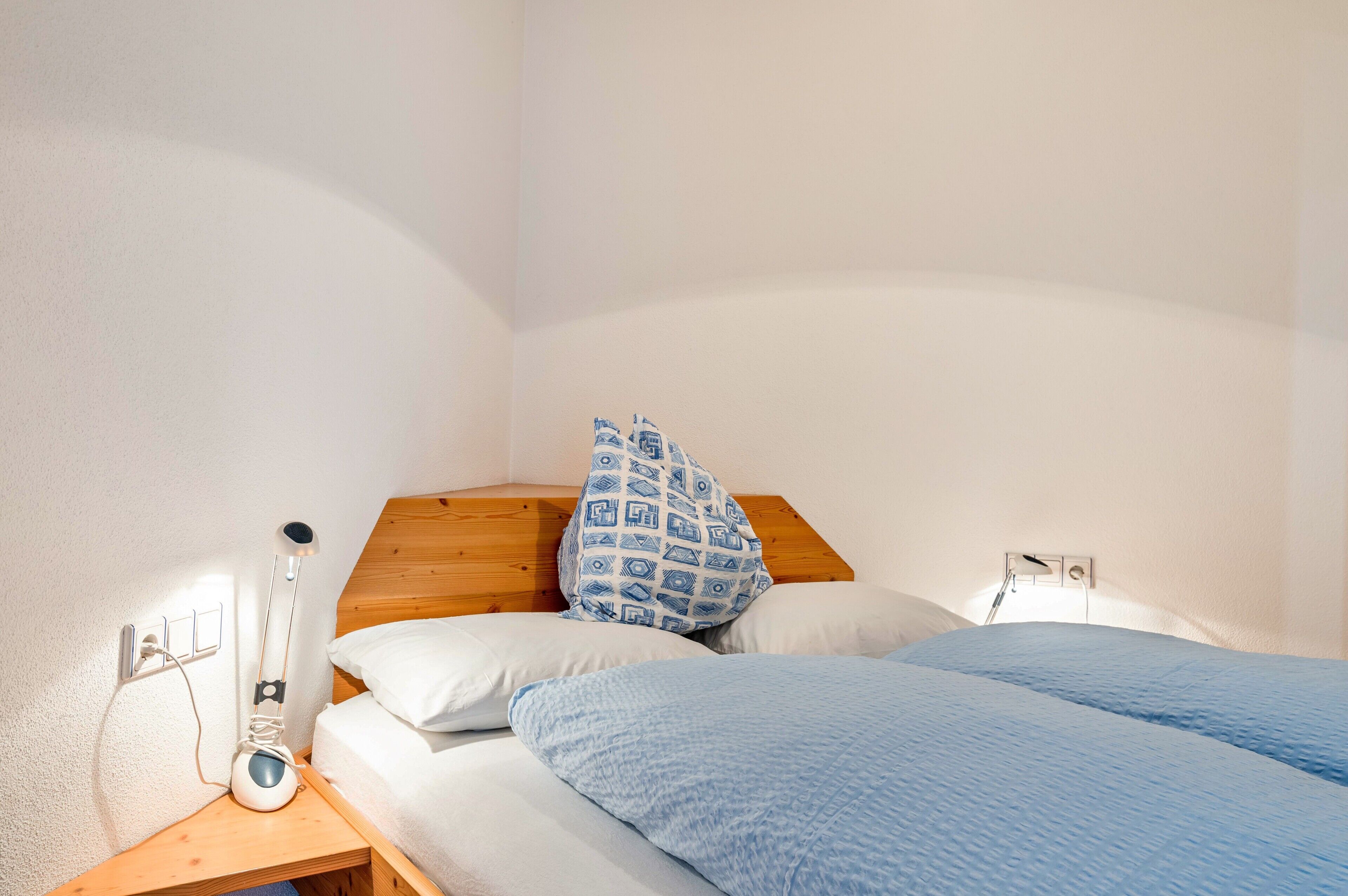 Un dormitorio con cabecera de madera, una mesita de noche con lámpara y cama con ropa de cama azul.