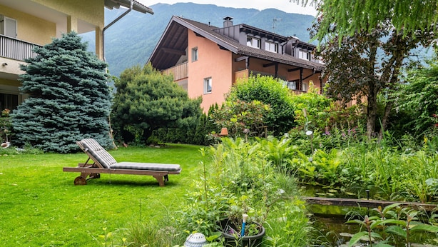 A garden with a pool, a lounge chair, and a building with balconies.