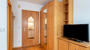 A hallway with wooden cabinets, a television on a stand, and a door leading to a bathroom.