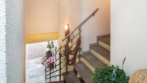 Eine Treppe mit Metallgeländer, einer Wandleuchte und Pflanzen in Töpfen auf dem Zwischenpodest.