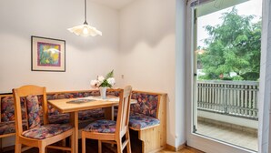 Ein Essbereich mit Holztisch und Sitzbank, einem gerahmten Kunstwerk an der Wand und Blick auf einen Balkon mit Geländer.