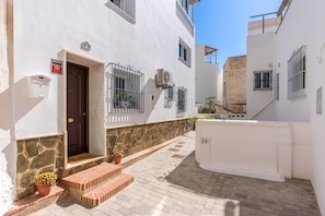 A narrow street with white buildings, a stone wall, and a door with a mailbox.