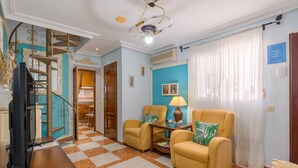 Una sala de estar con suelo a cuadros, dos sillones amarillos, una mesa de centro, un televisor y una escalera.