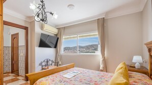 Habitación de hotel con cama, televisión, ventana con vistas y un candelabro.