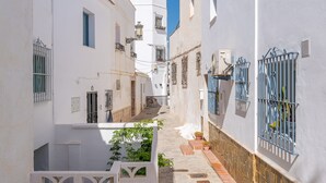 Una calle estrecha con edificios blancos, rejas azules en las ventanas y un cielo azul despejado.