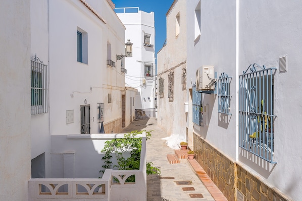 A narrow street with white buildings, blue window bars, and a clear blue sky.