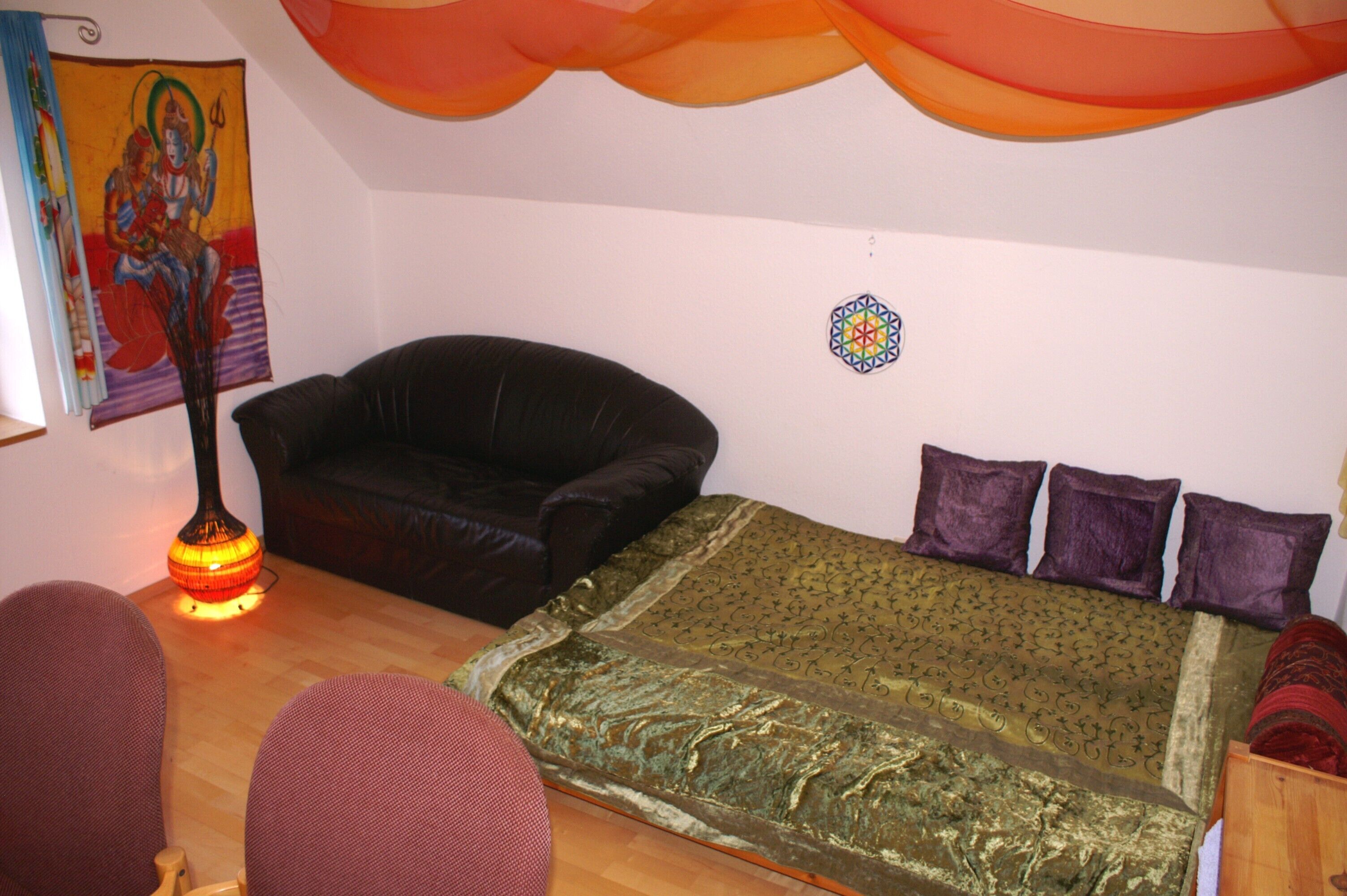 Ein Zimmer mit einem Bett, einer schwarzen Ledersofa, einem kleinen Tisch und einer Wanddekoration.