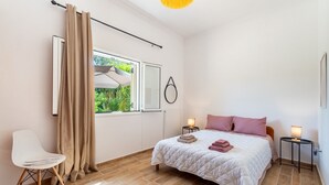 Una camera da letto con un letto, comodini, una sedia, una finestra con tende e una lampada a sospensione.