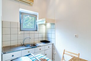 Una cucina compatta con finestra, lavello, piano di lavoro e una sedia.