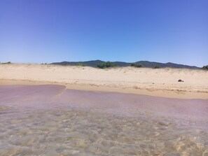 Platja d'aigua cristal·lina, sorra daurada i turons allunyats.