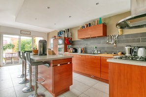 A modern kitchen with a central island, bar stools, wooden cabinets, and a built-in stove.