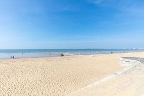 A wide sandy beach with a clear sky and calm sea.