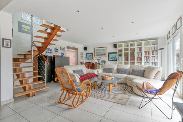A modern living room with a wooden staircase, a sofa set, a coffee table, and a bookshelf.