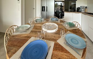 Enjoy meals in this dining area with a round table and wicker chairs, surrounded by glassware and a decorative centerpiece.
