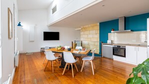 A modern kitchen with white cabinets, a blue accent wall, and a dining area with a wooden table and white chairs.
