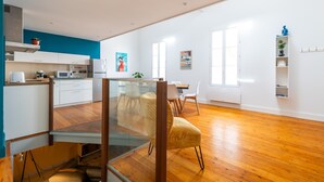 A modern kitchen with white cabinets, a glass dining table, and a wooden floor.